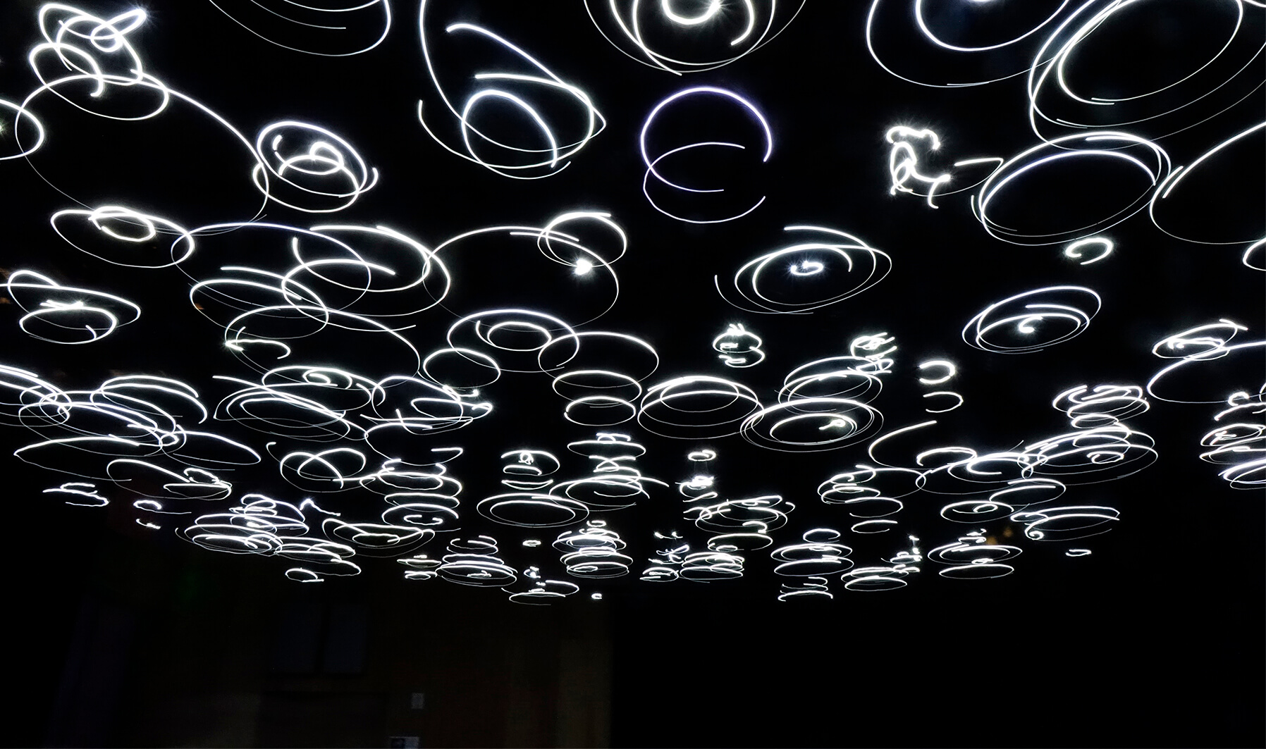 Entangled Attraction Image of lights that are spinning and seem to leave a trail of glowing light as they spin. The background is very dark, making the lights look as though they are hovering.